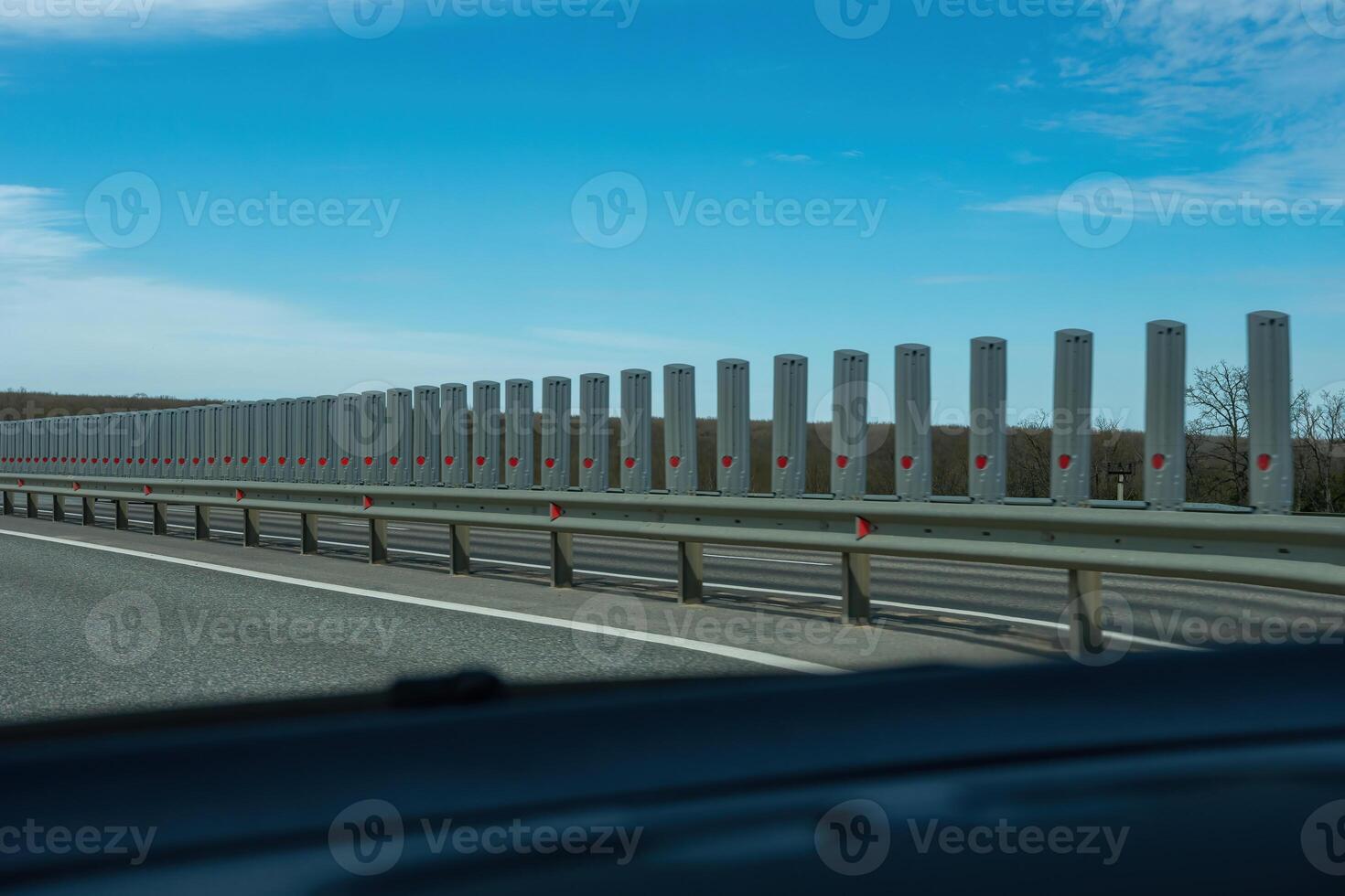 A road with a long line of metal posts with red hearts on them. The road is empty and the sky is clear. photo