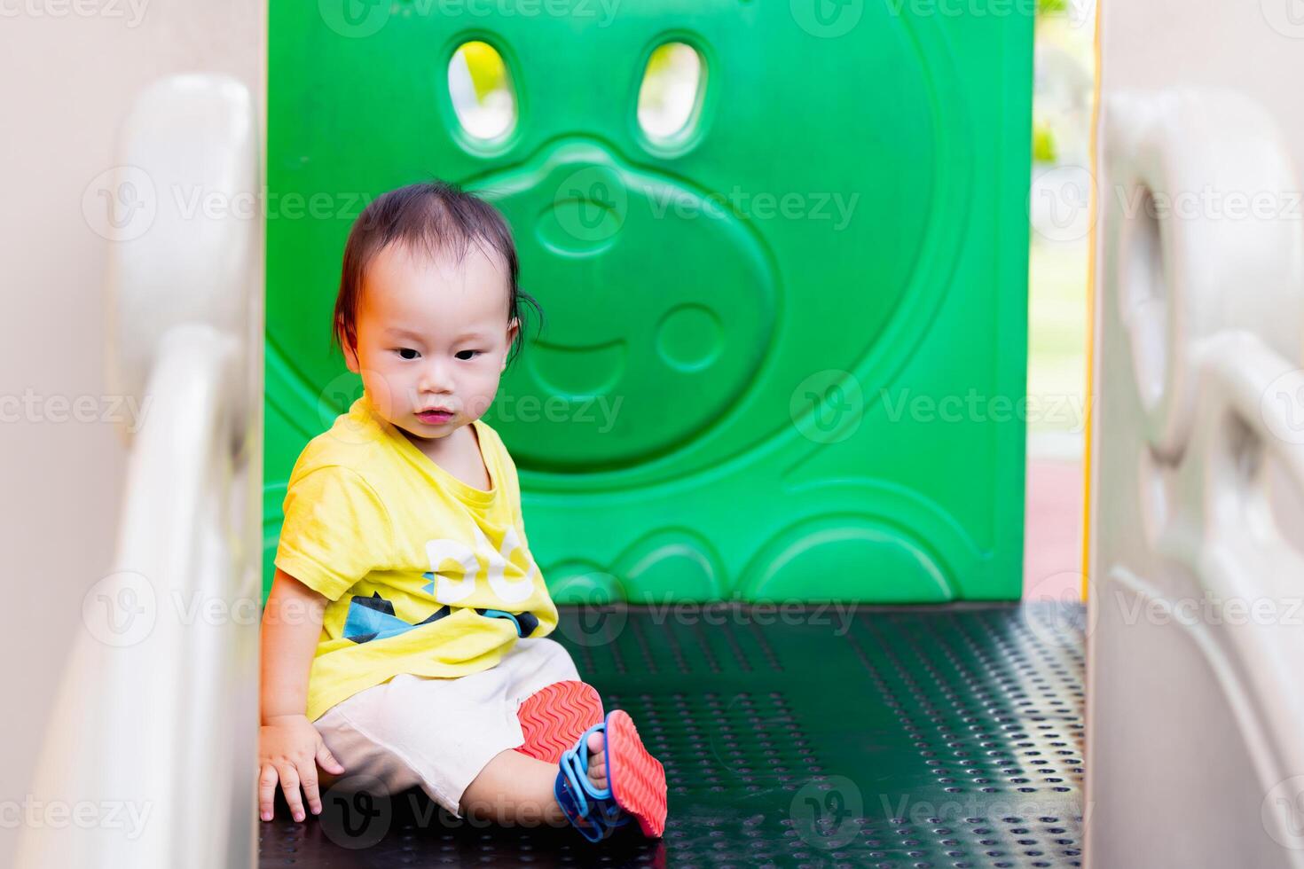 Portrait of an Asian boy sitting on a playground equipment, in the summer or spring time, a young child is sweating due to the very hot weather, a one-year-old cute toddler. Copy space. photo