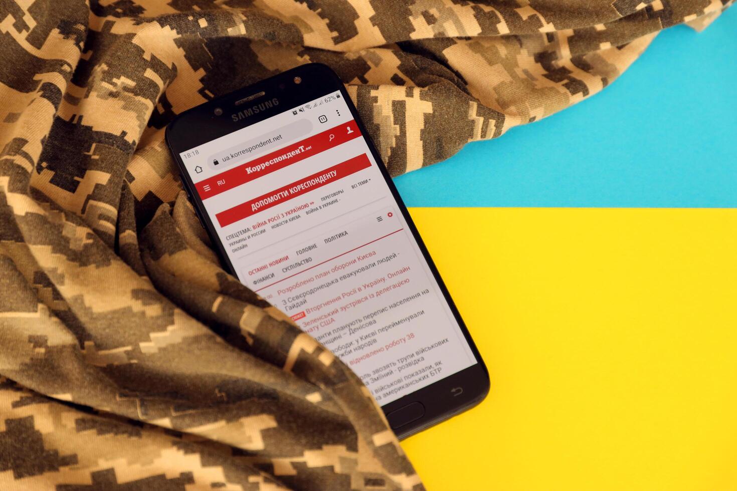 KYIV, UKRAINE - 4 MAY, 2023 Correspondent ukrainian news portal on smartphone screen with ukrainian flag and camouflage fabric photo