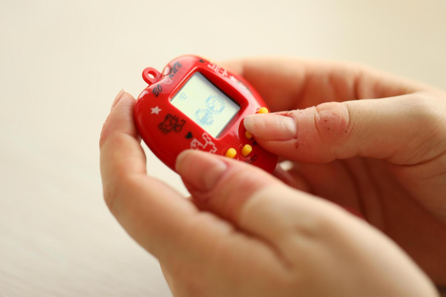 KYIV, UKRAINE - MARCH 9, 2024 Retro pet keychain game tamagotchi in red plastic case in female hands photo