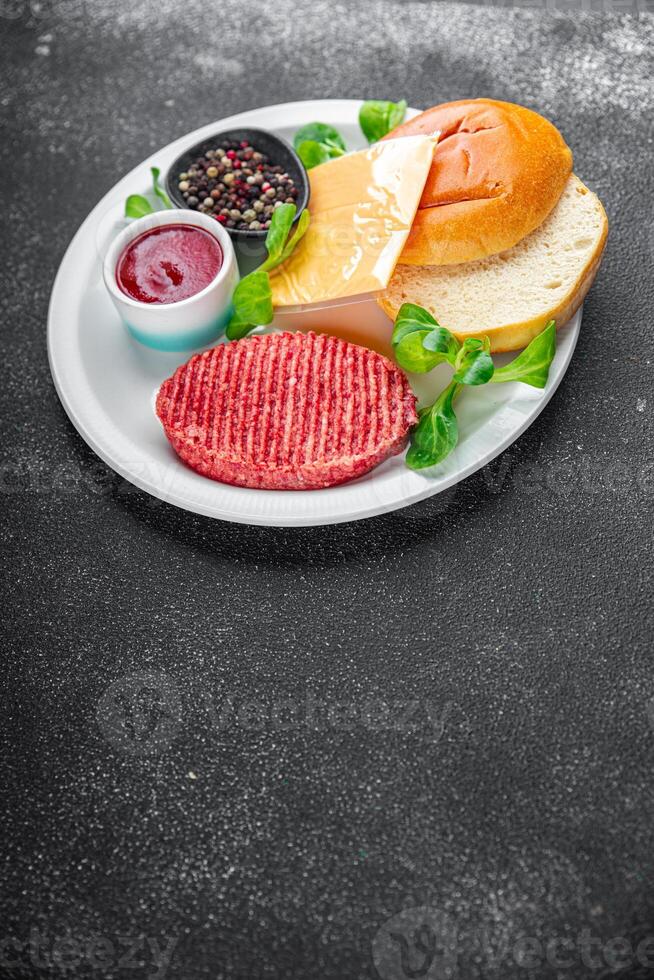 crudo hamburguesa conjunto chuleta, bollo, queso, tomate salsa, verduras Fresco Cocinando comida comida bocadillo en el mesa Copiar espacio comida antecedentes foto