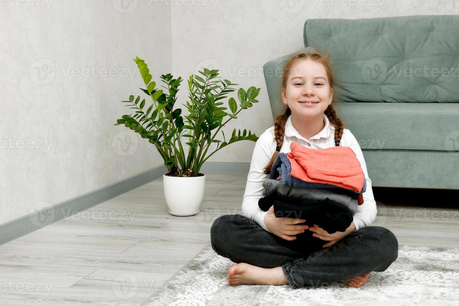 cute little girl holding a stack of clothes in her hands while sitting on the floor photo