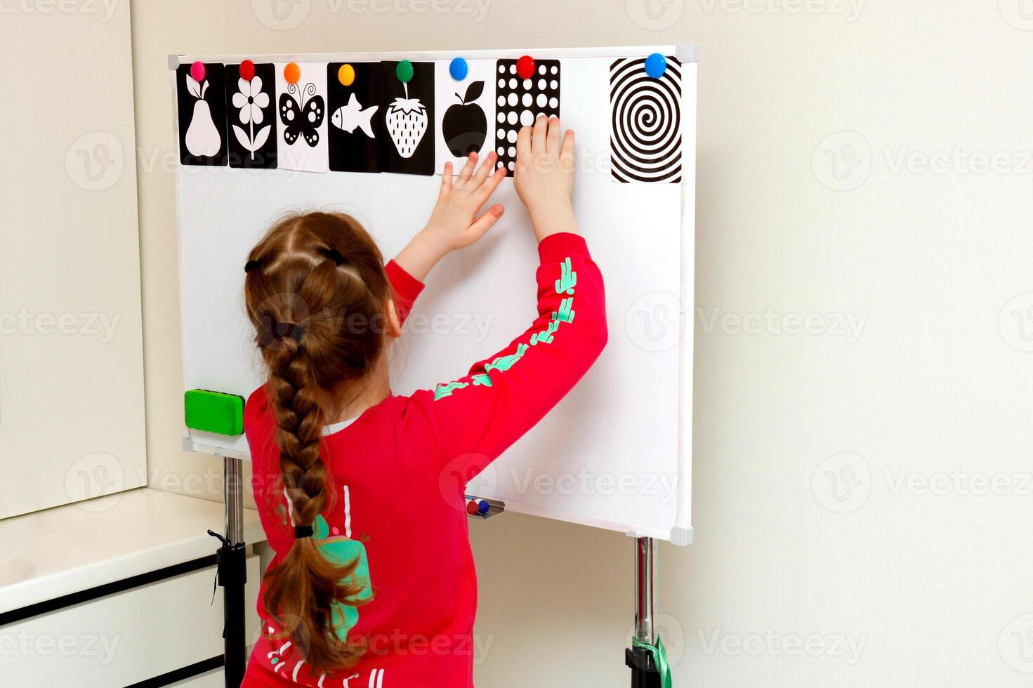 pequeño niña colgando negro y blanco tarjetas en un magnético tablero foto