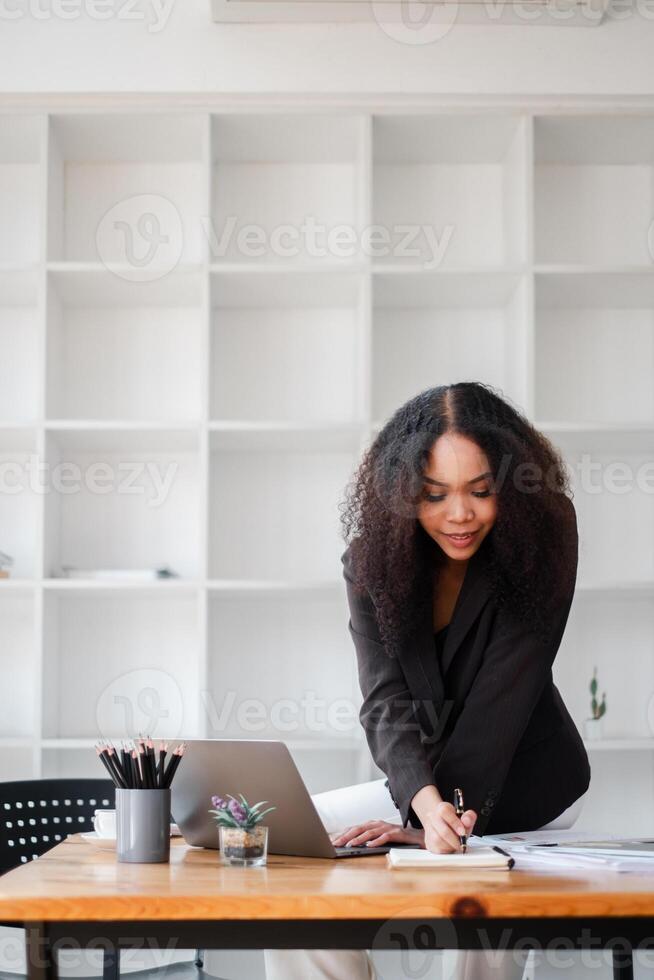 A woman is sitting at a desk with a laptop and a notebook photo