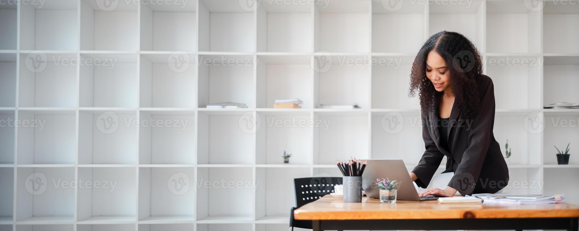 Businesswoman in a dark blazer works intently on a laptop at a modern office desk. photo