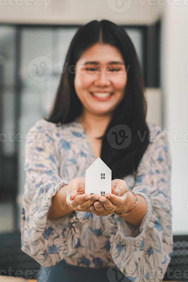 Beaming woman holding out a small model of a house, representing homeownership or real estate business. photo