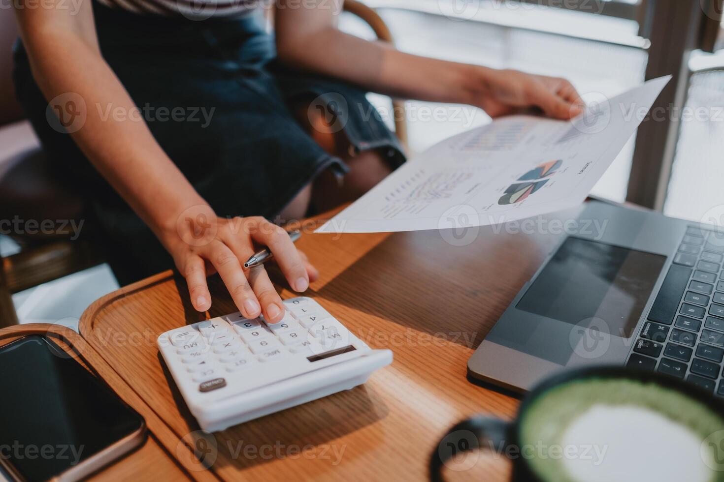 Professional conducting financial calculations using a calculator and reviewing colorful data graphs, with laptop and smartphone in view. photo