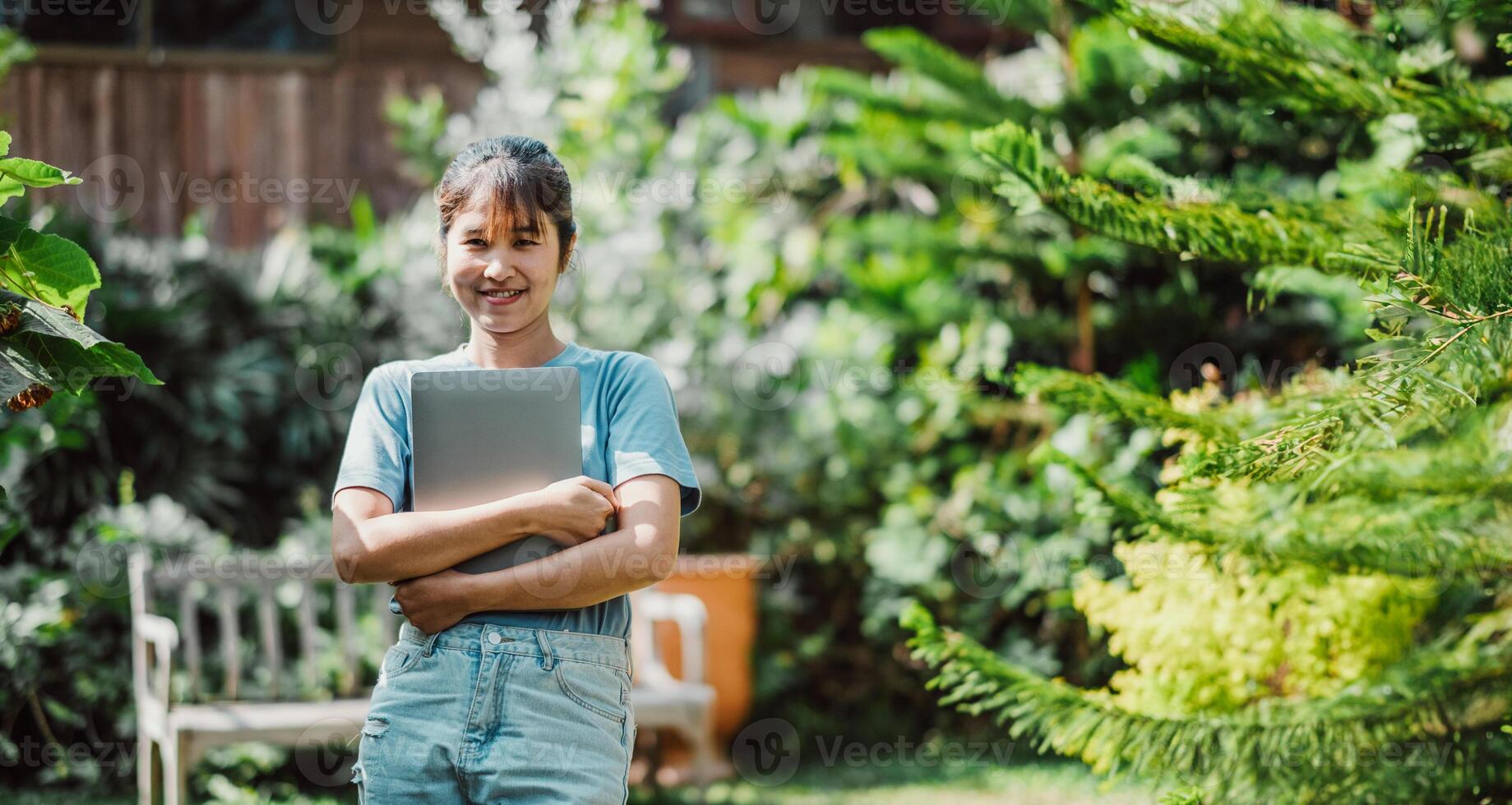 Smiling woman holding a laptop, standing in a lush garden, symbolizing work-life balance and remote work flexibility. photo