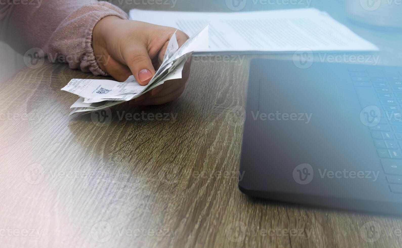A man holds receipts from shops in front of a laptop. photo