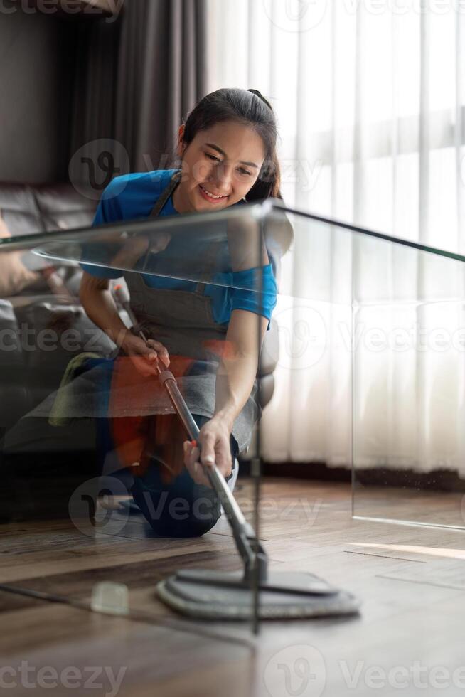 Asian cleaning service woman worker cleaning in living room at home. Beautiful young girl housekeeper cleaner wear apron and wipe messy dirty floor for housekeeping housework in house photo