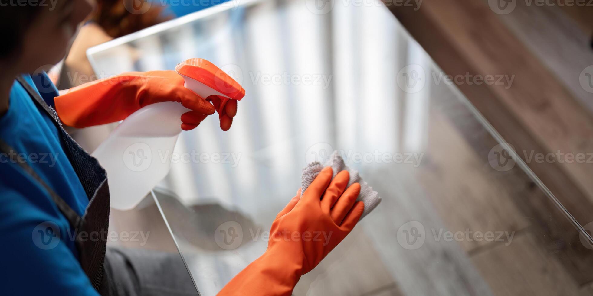 asiático mujer limpieza el vaso mesa en el departamento. limpieza personal mantener limpieza en con toalla y rociar detergente foto
