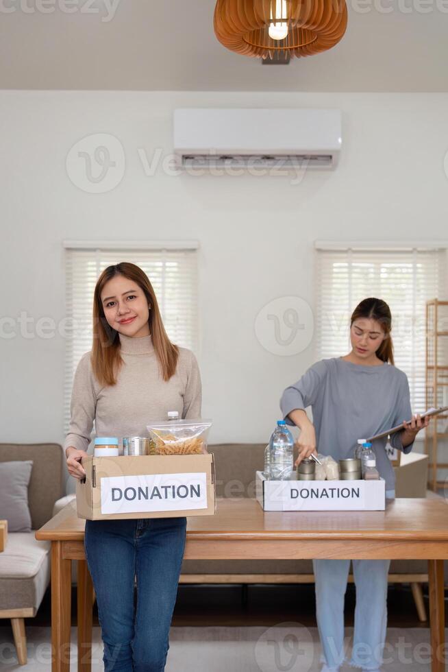 Donation and two woman volunteer asian of happy packing food in box at home. Charity photo