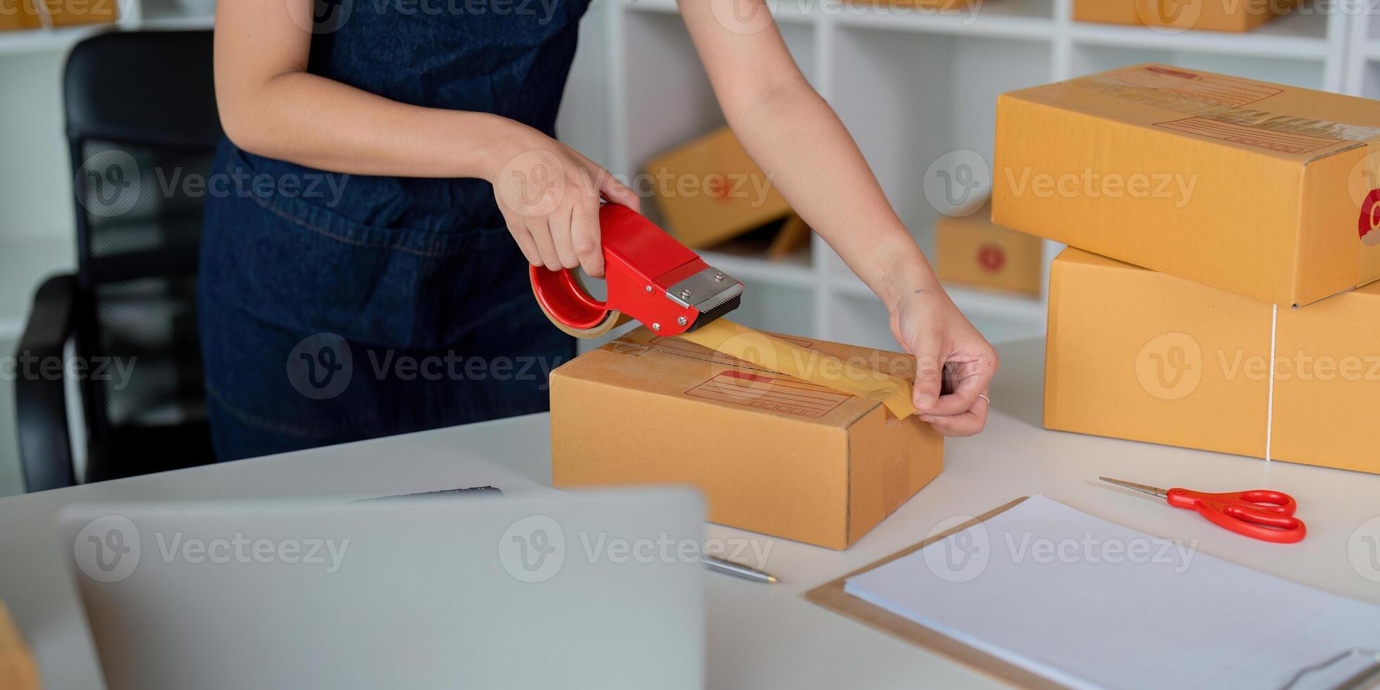 Woman use scotch tape to attach parcel boxes to prepare goods for the process of packaging at home, shipping, online sale internet marketing ecommerce concept startup business idea photo