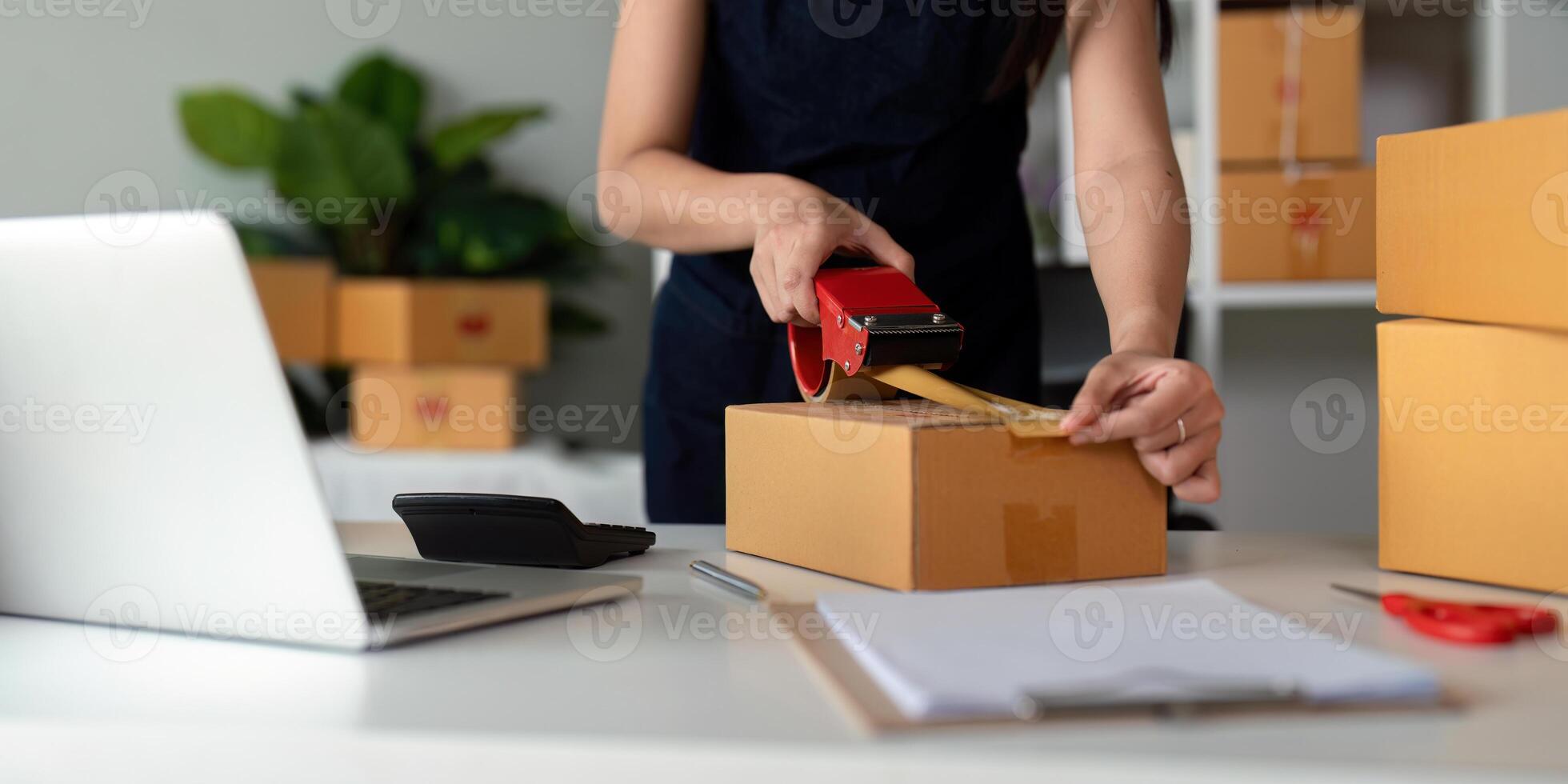 Woman use scotch tape to attach parcel boxes to prepare goods for the process of packaging at home, shipping, online sale internet marketing ecommerce concept startup business idea photo
