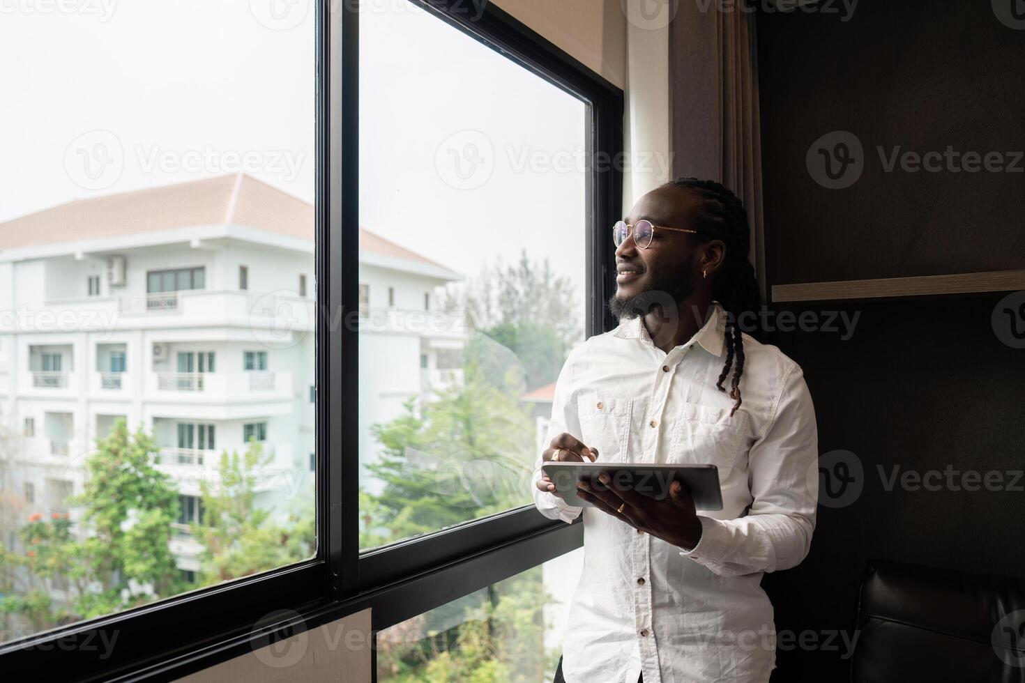 Happy young African business man using online app on tablet for job communication, looking out the window photo