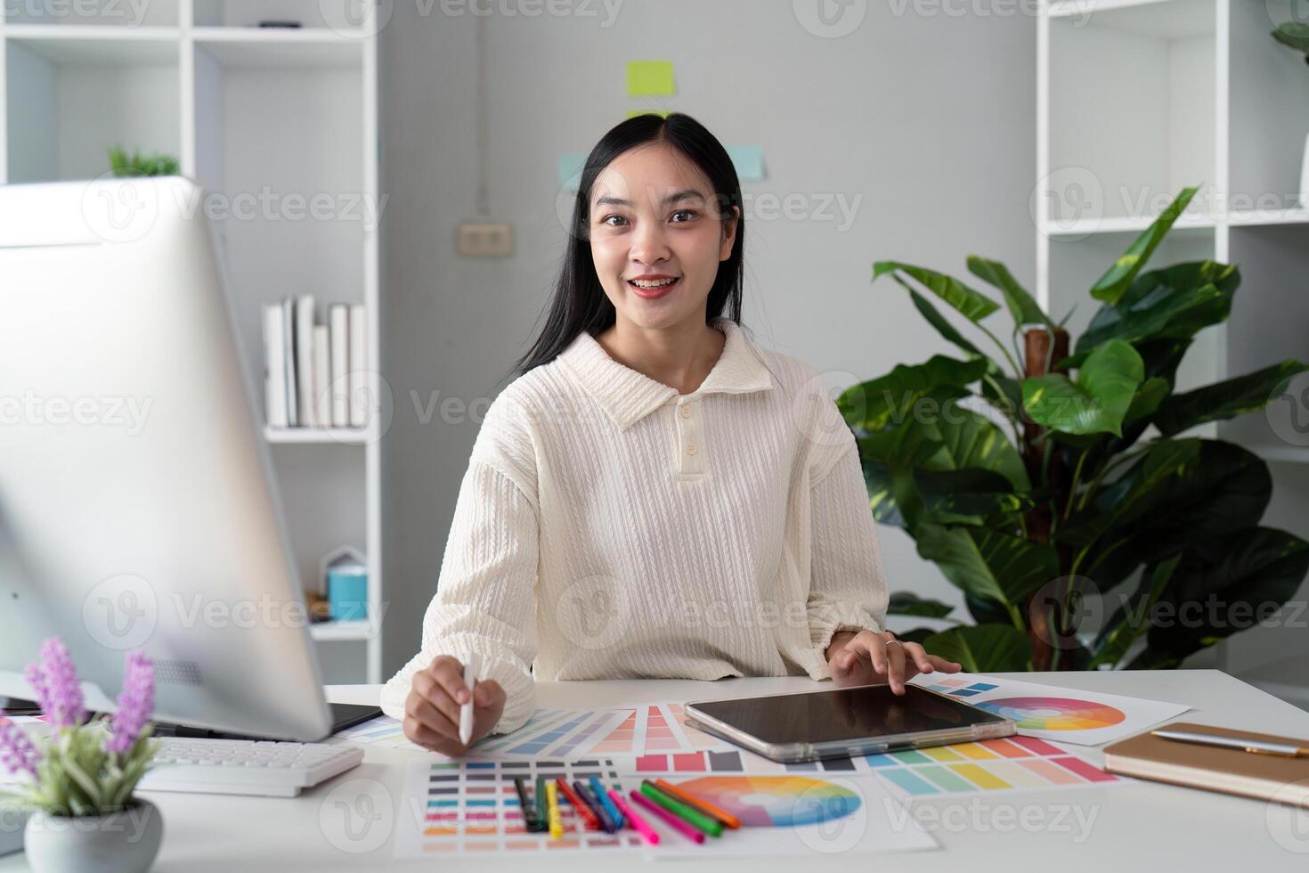Asian woman freelance graphic designer working with color swatch samples and computer at desk in home office, young lady choosing color gamma for new design project photo