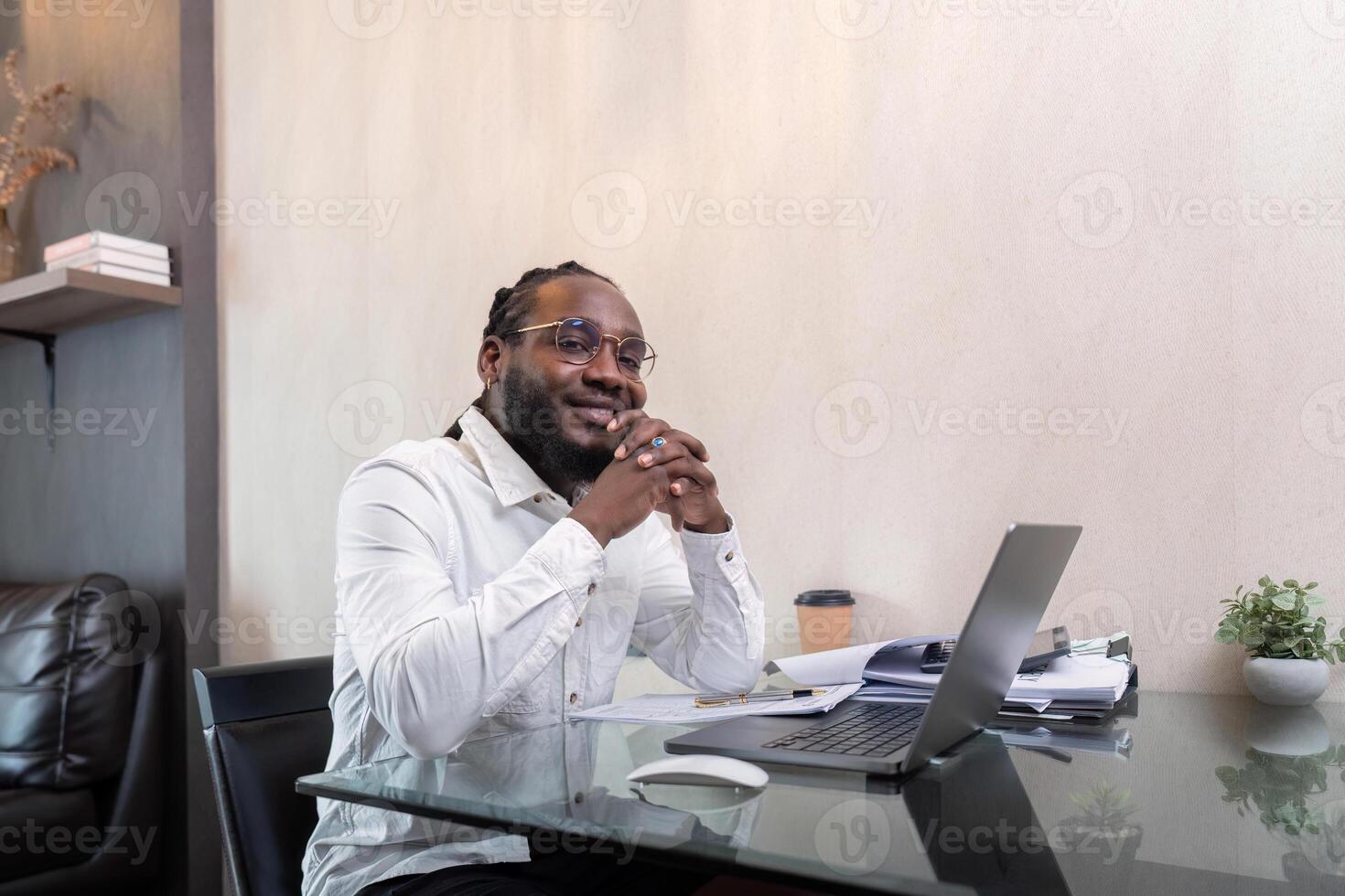 Smiling African American man sit at desk in home working on laptop, happy African American male look at camera posing, busy using modern computer gadget at home photo