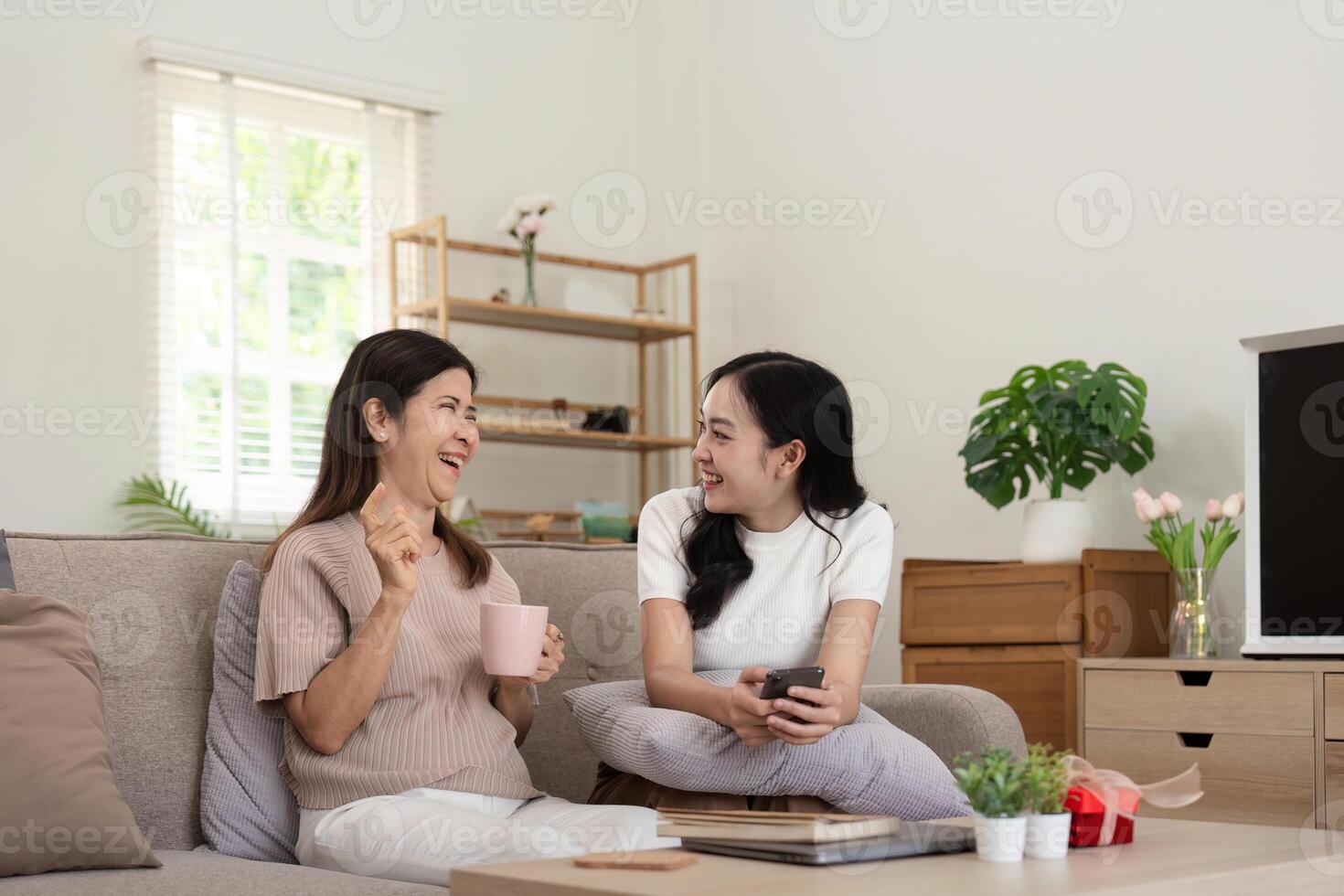 Happy senior mother with adult daughter sitting on couch and holding cups with coffee or tea at home. Enjoy family concept photo
