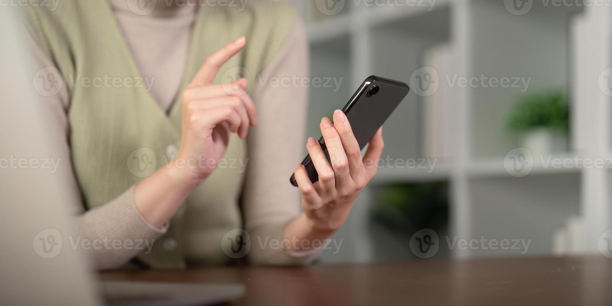 Young business woman using mobile phone, working on laptop computer at home. Female freelancer online working, using smartphone surfing the internet, remote work photo