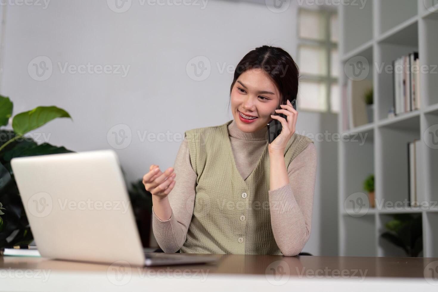 Happy beautiful asian woman relaxing using of laptop computer while sitting on table. Young creative girl working and talk on the phone at home. work at home concept photo