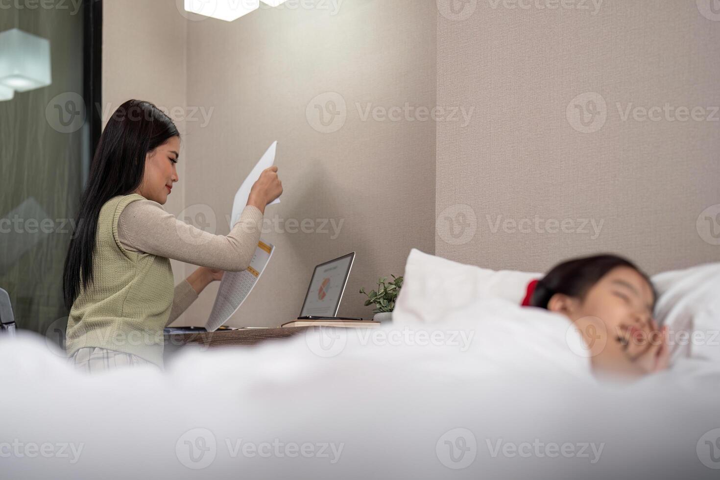 asiático madre trabajando en cama con dormido hija por lado a hogar foto