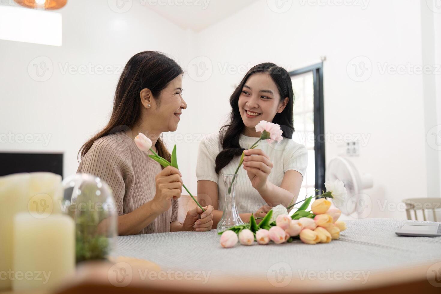 mayor madre y adulto hija contento en el mesa mientras organizar flores en un florero juntos. tecnología y estilo de vida concepto. contento hora juntos foto