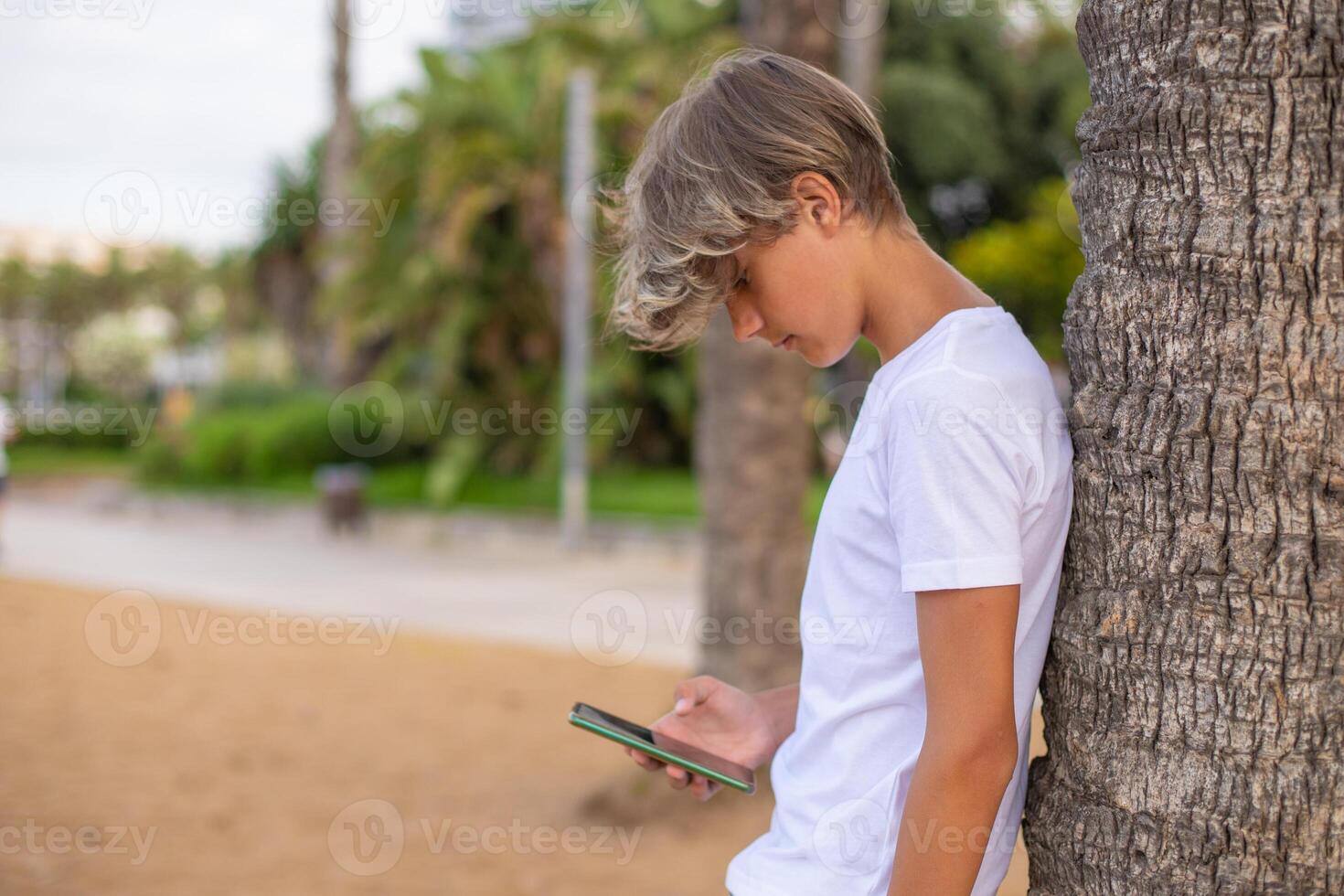 Close up handsome teenager boy using mobile phone outdoors in a park, copy space.Side view. photo