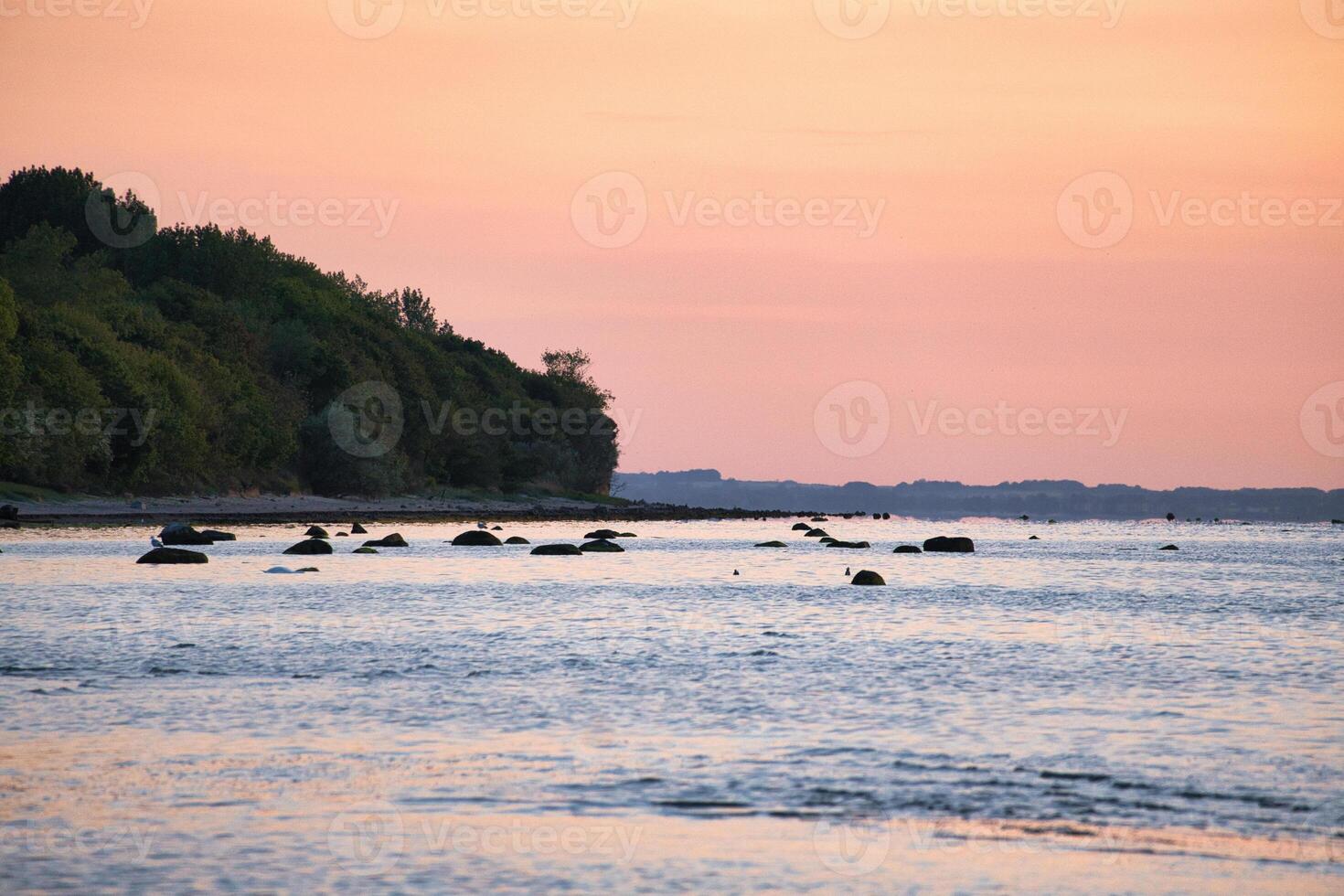 Sunset, illuminated sea. Sandy beach in the foreground. Light waves. Baltic Sea photo
