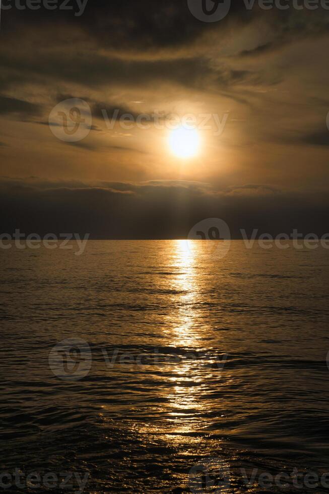 Sunset, illuminated sea. A few clouds in the sky, light waves rolling onto the beach photo