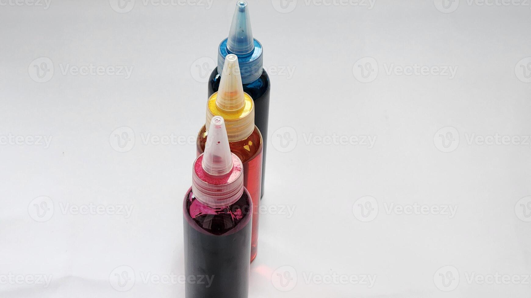 three different colored ink bottles are lined up on a white surface photo