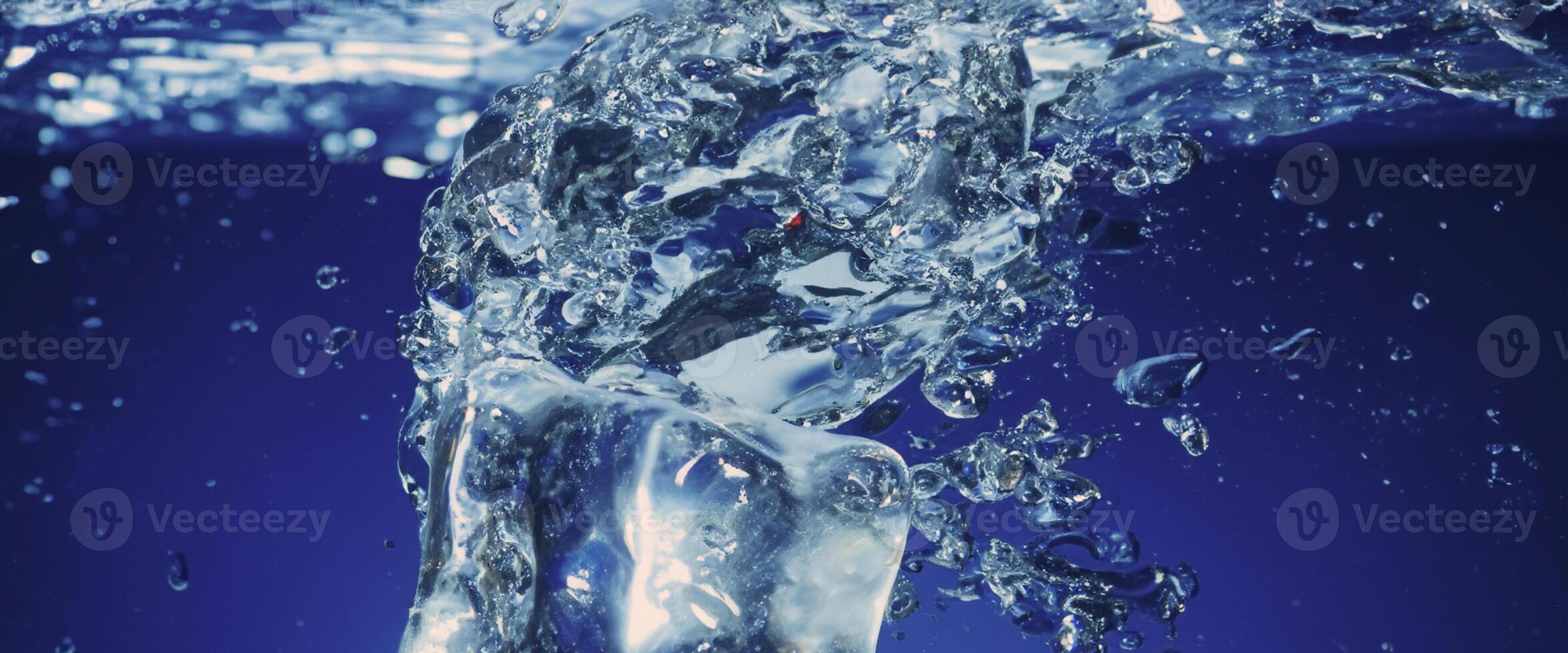 Water splashing and ice cube. Ice splashing into a glass of water. Underwater pouring ice cubes falling into clear watering background. Refreshing chill drinking. Ices in a glass with blue background photo