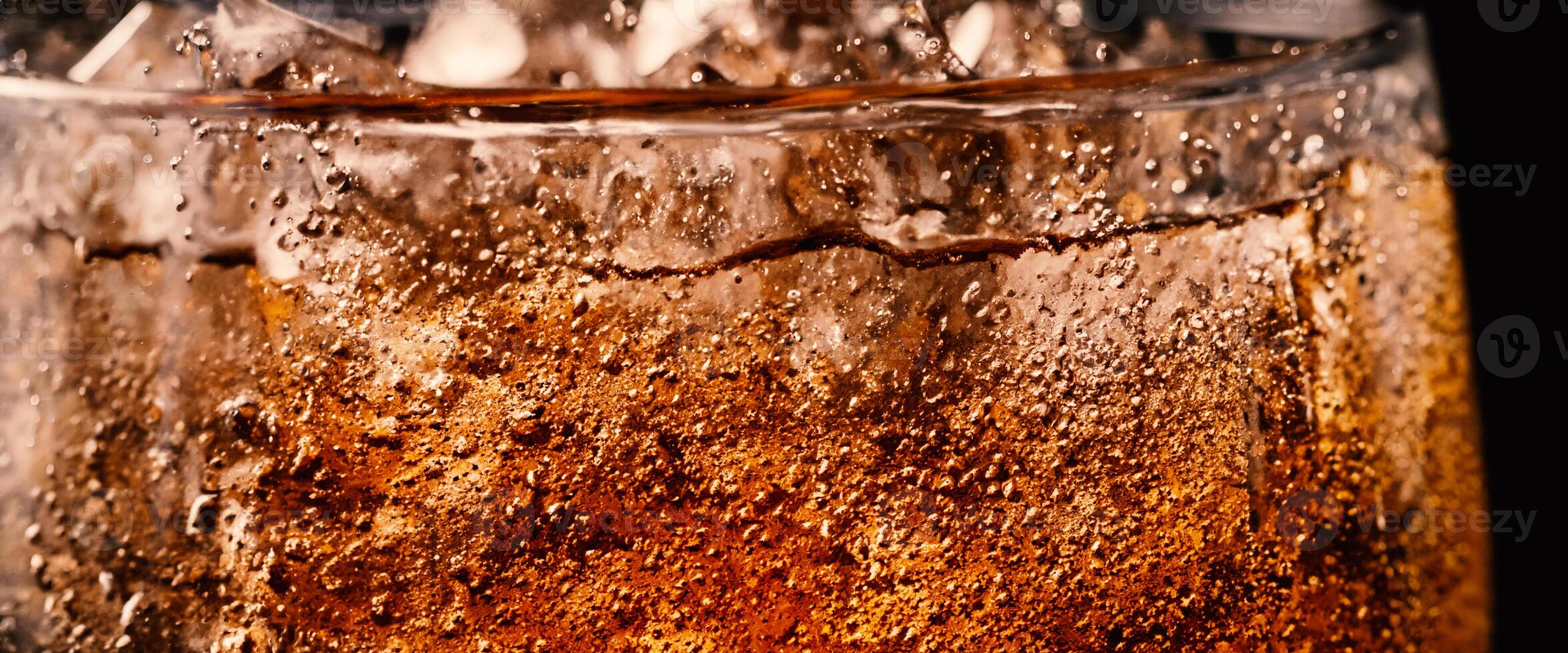 Splashing of Cola and Ice. Cola soda and ice splashing fizzing or floating up to top of surface. Close up of ice in cola water. Texture of carbonate drink with bubbles in glass. Cold drink background photo