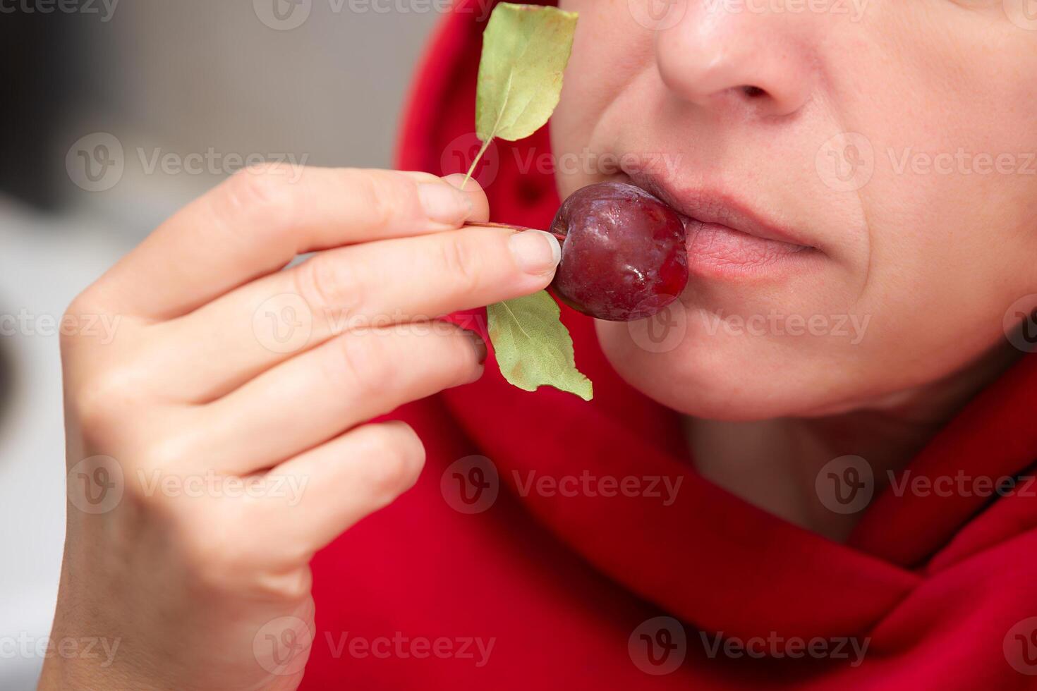 A woman, whose face is not visible, eats a small red wild apple. photo