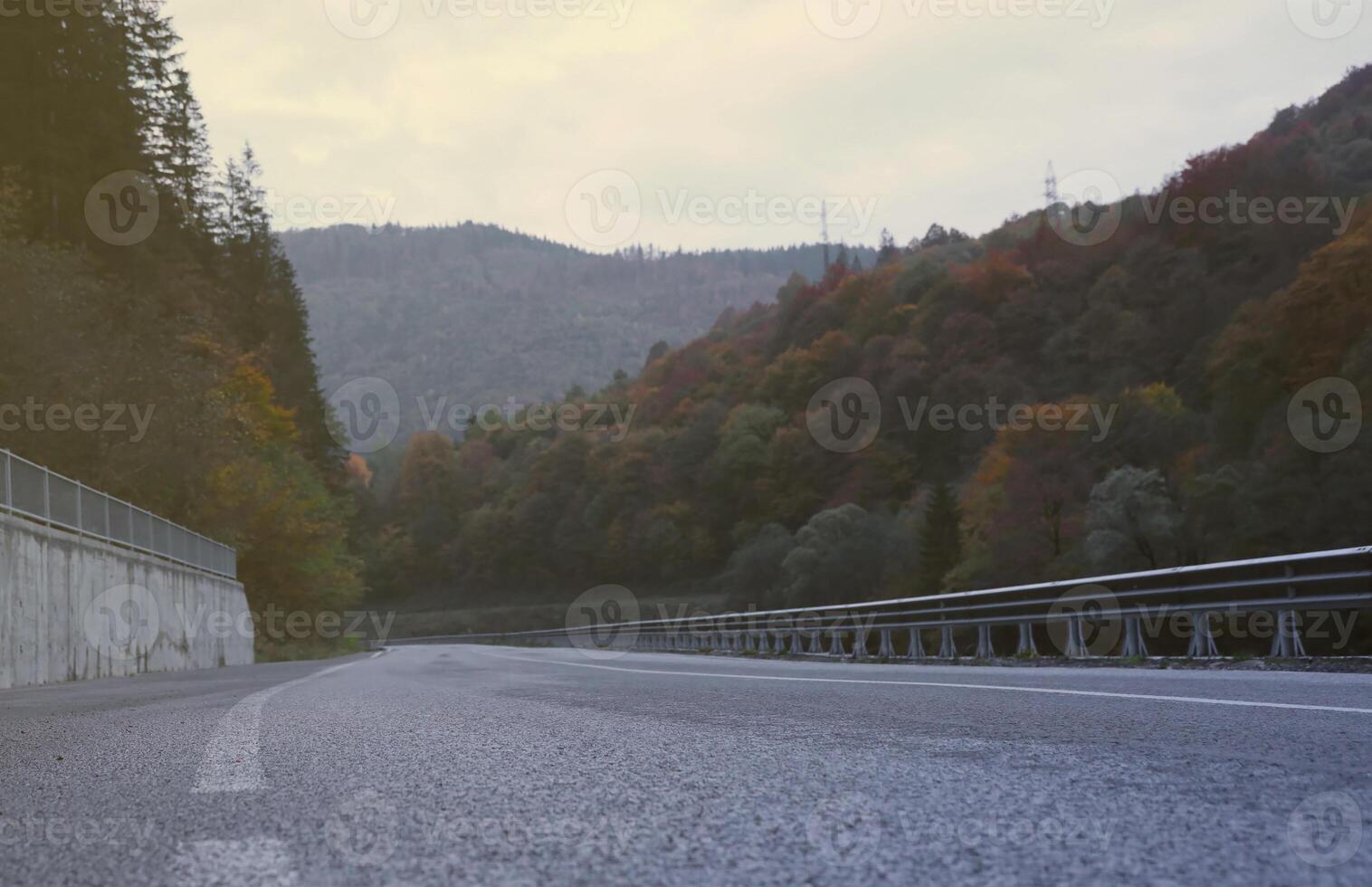 Road in autumn forest at sunset in Carpathian mountains, Ukraine. Beautiful mountain roadway with orange tress and high rocks. Landscape with empty highway through the woods in fall photo