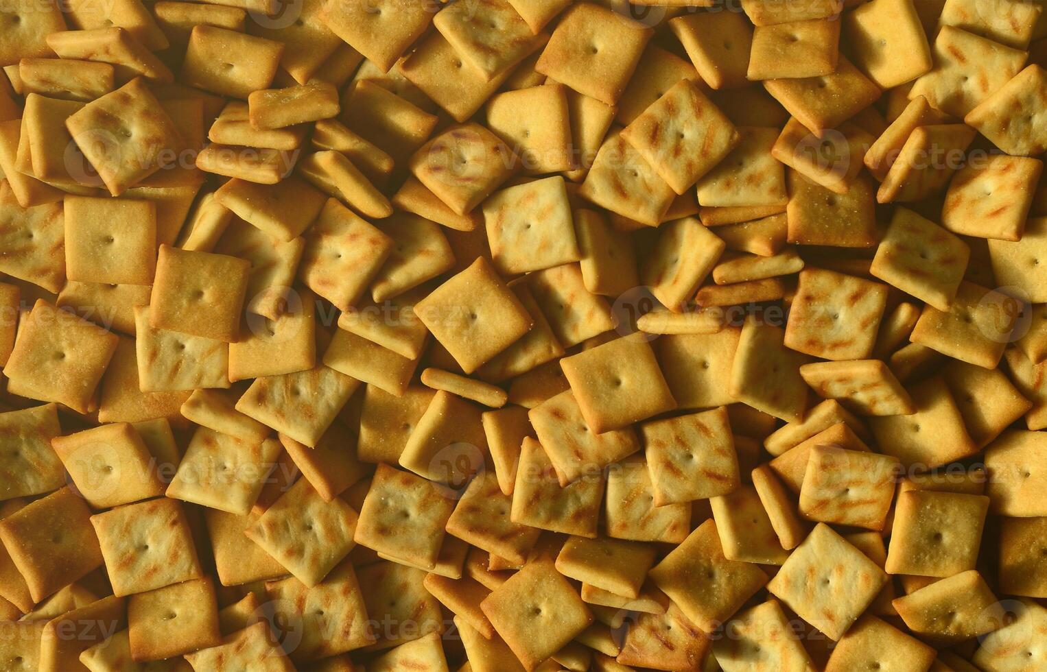 A lot of small cookies are square shaped. A pattern of a yellow salt cracker. Background image with salted pastry photo