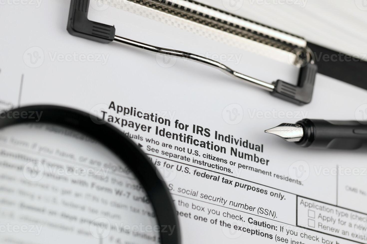 IRS Form W-7 Application for IRS Individual taxpayer identification number blank on A4 tablet lies on office table with pen and magnifying glass photo