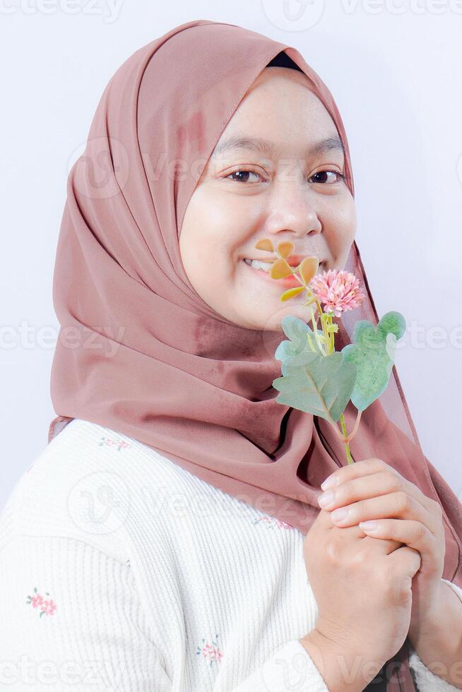 woman in hijab kissing plastic flowers on white background with empty space for photocopy. photo