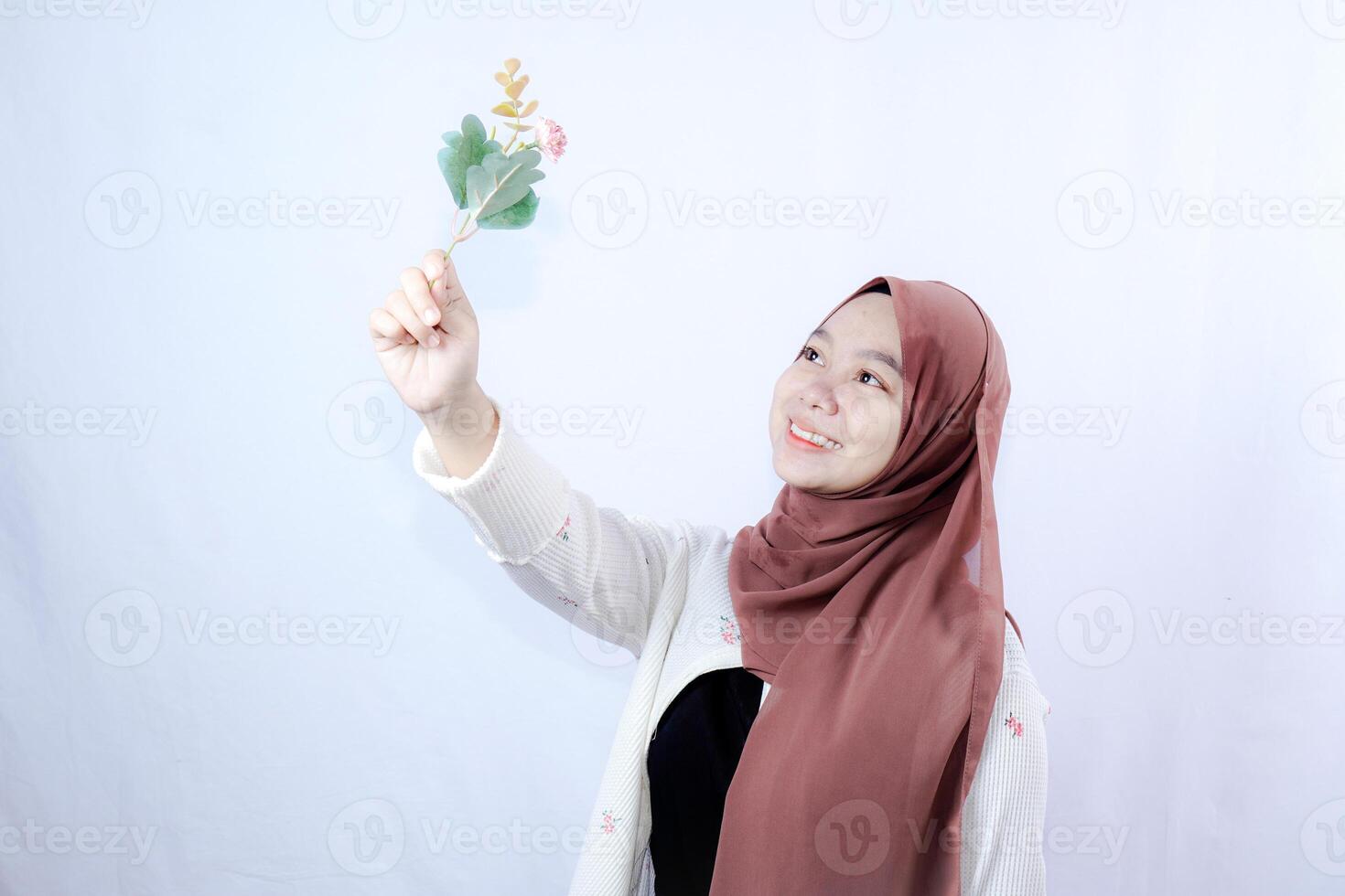 a veiled Javanese woman is looking at a flower held up in her hand against the background of an empty space for photocopying. photo