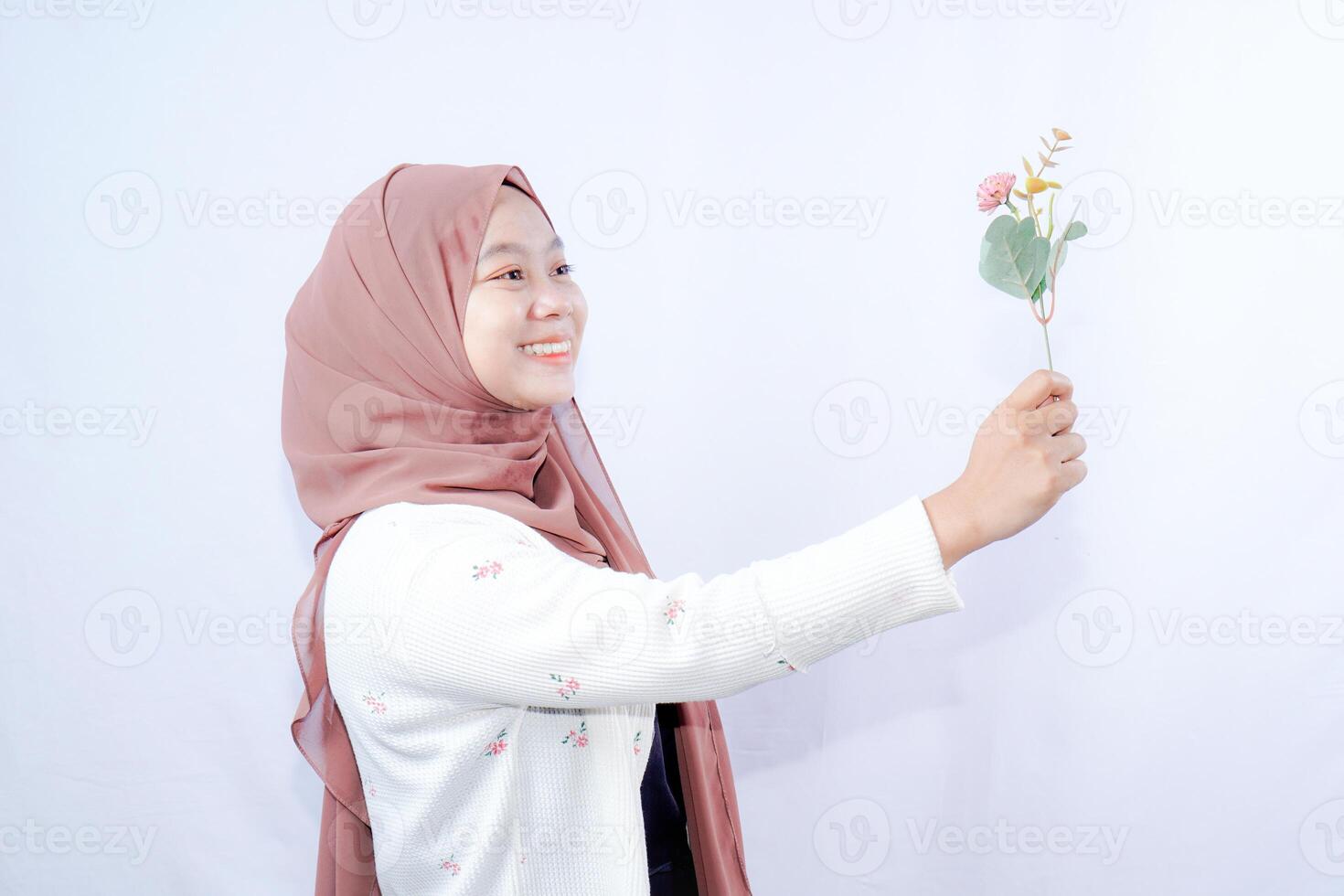 a veiled Javanese woman is looking at a flower held up in her hand against the background of an empty space for photocopying. photo