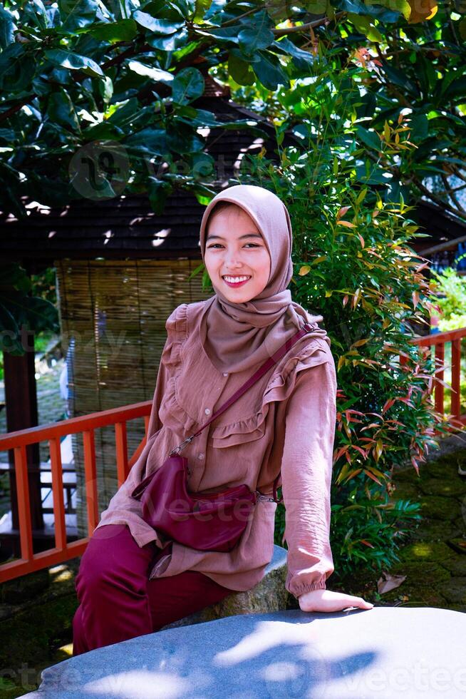 a woman wearing a headscarf sitting in the garden with a background of trees as a photocopy space. photo