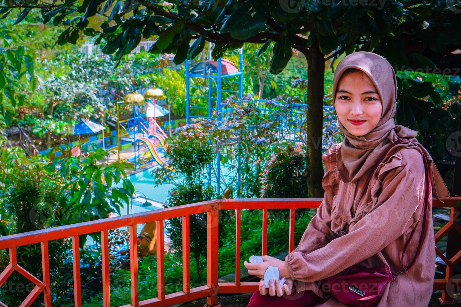 a woman wearing a headscarf sitting in the garden with a background of trees as a photocopy space. photo