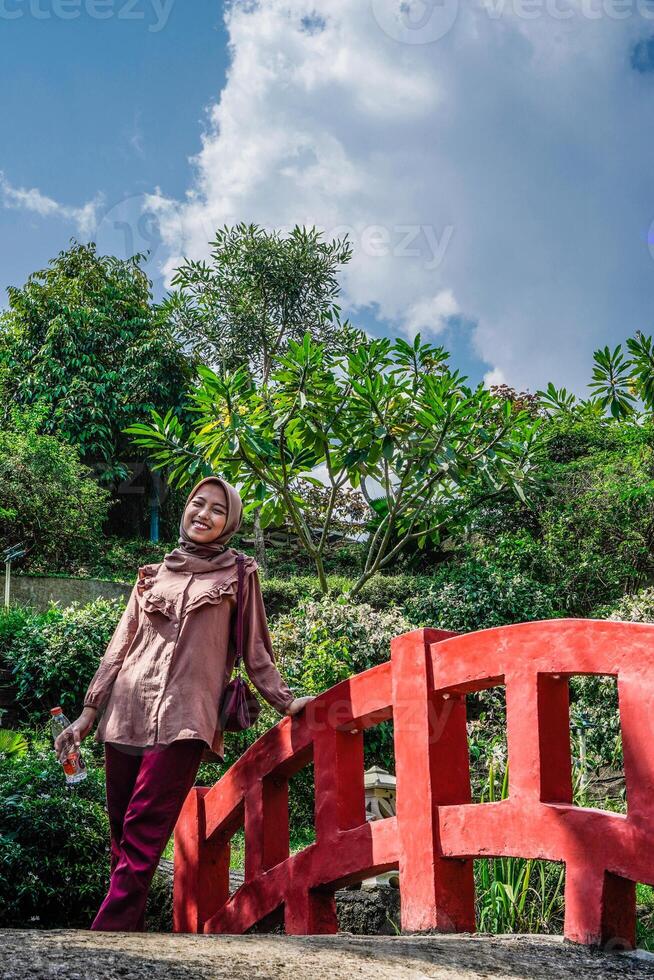 Muslim woman is standing on a bridge against a backdrop of trees with empty sky space for photocopying. photo