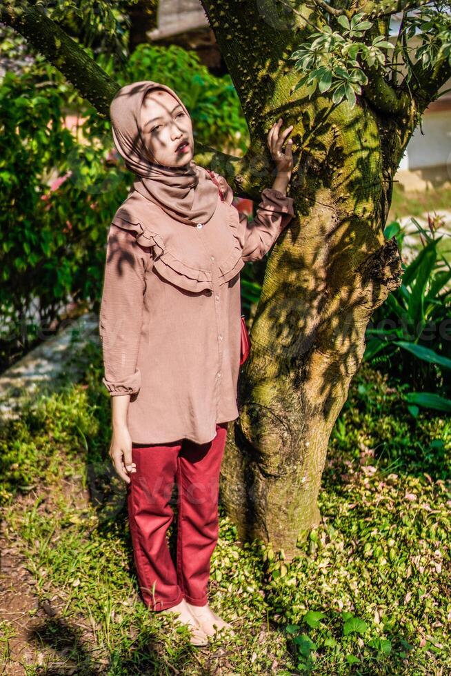 a veiled woman was standing next to a tree with the shadow of the leaves right on her face. photo