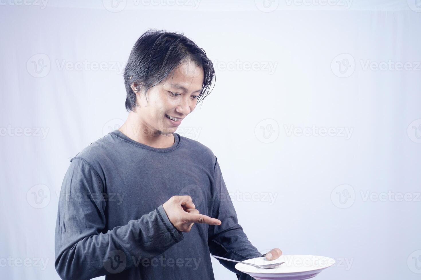 asian man pointing towards empty plate with happy expression isolated white background for coffee photo space. food menu presentation concept.