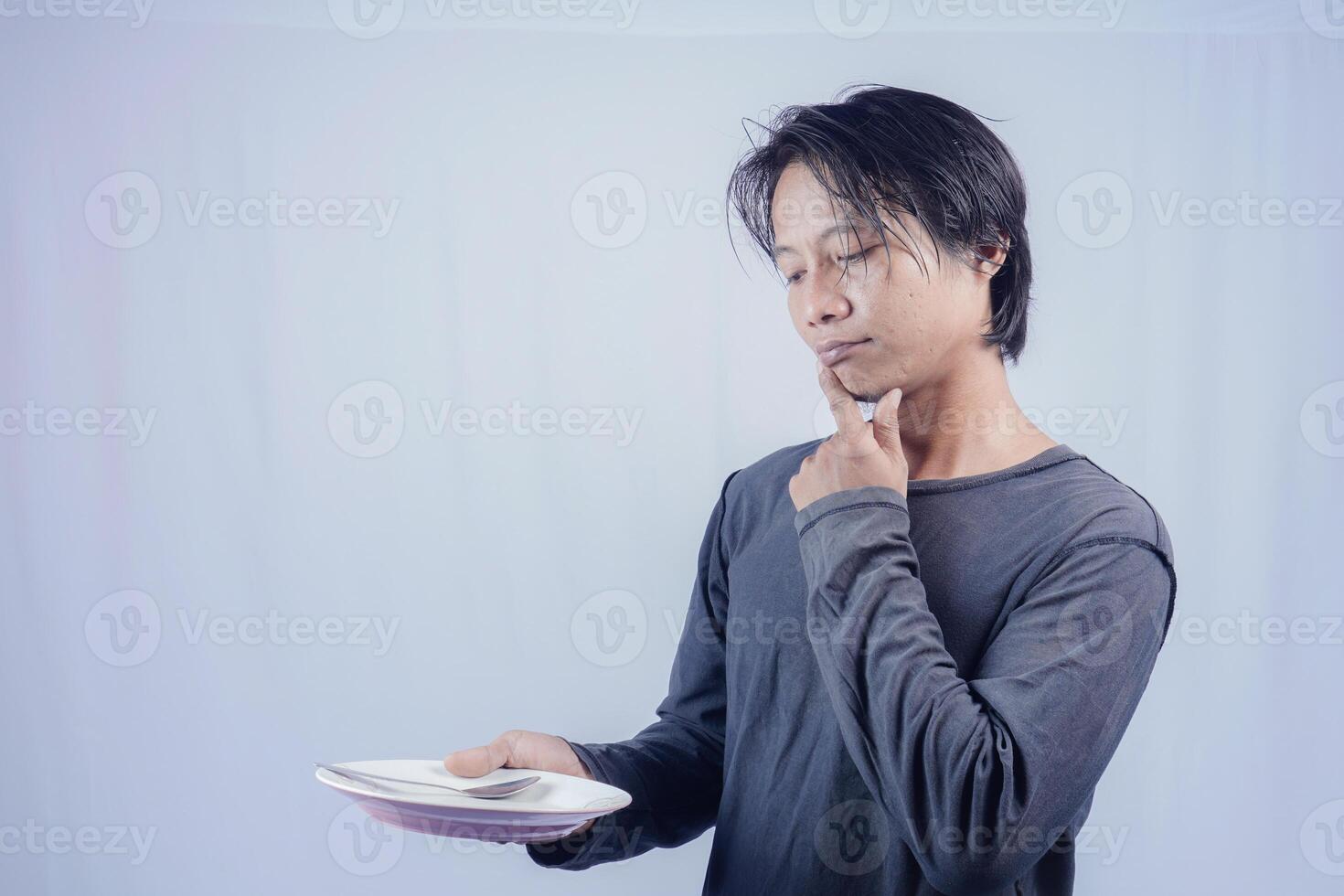 handsome asian man holding empty plate while thinking for serving food menu on isolated white background for advertising menu. menu presentation concept. photo