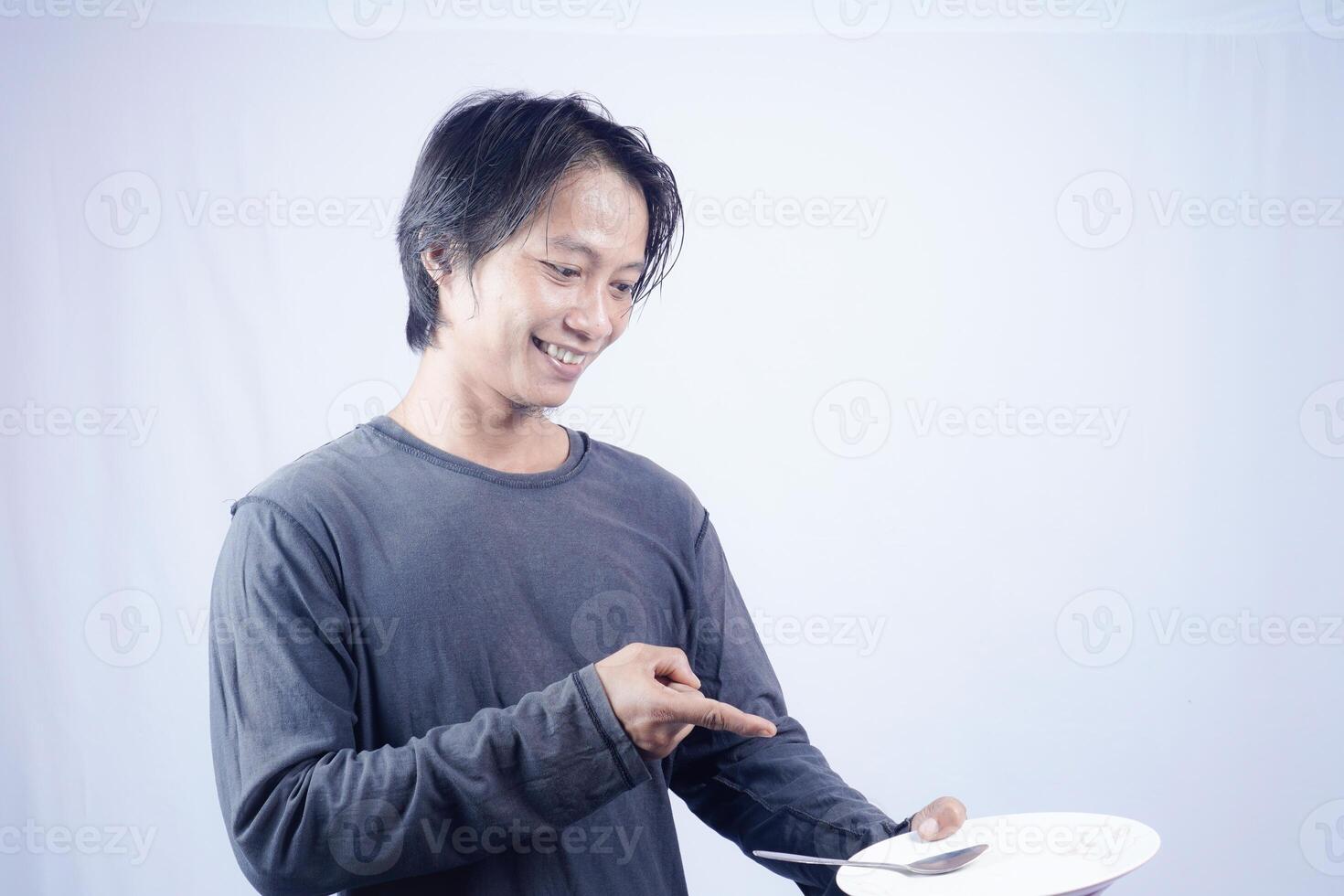 asian man pointing towards empty plate with happy expression isolated white background for coffee photo space. food menu presentation concept.