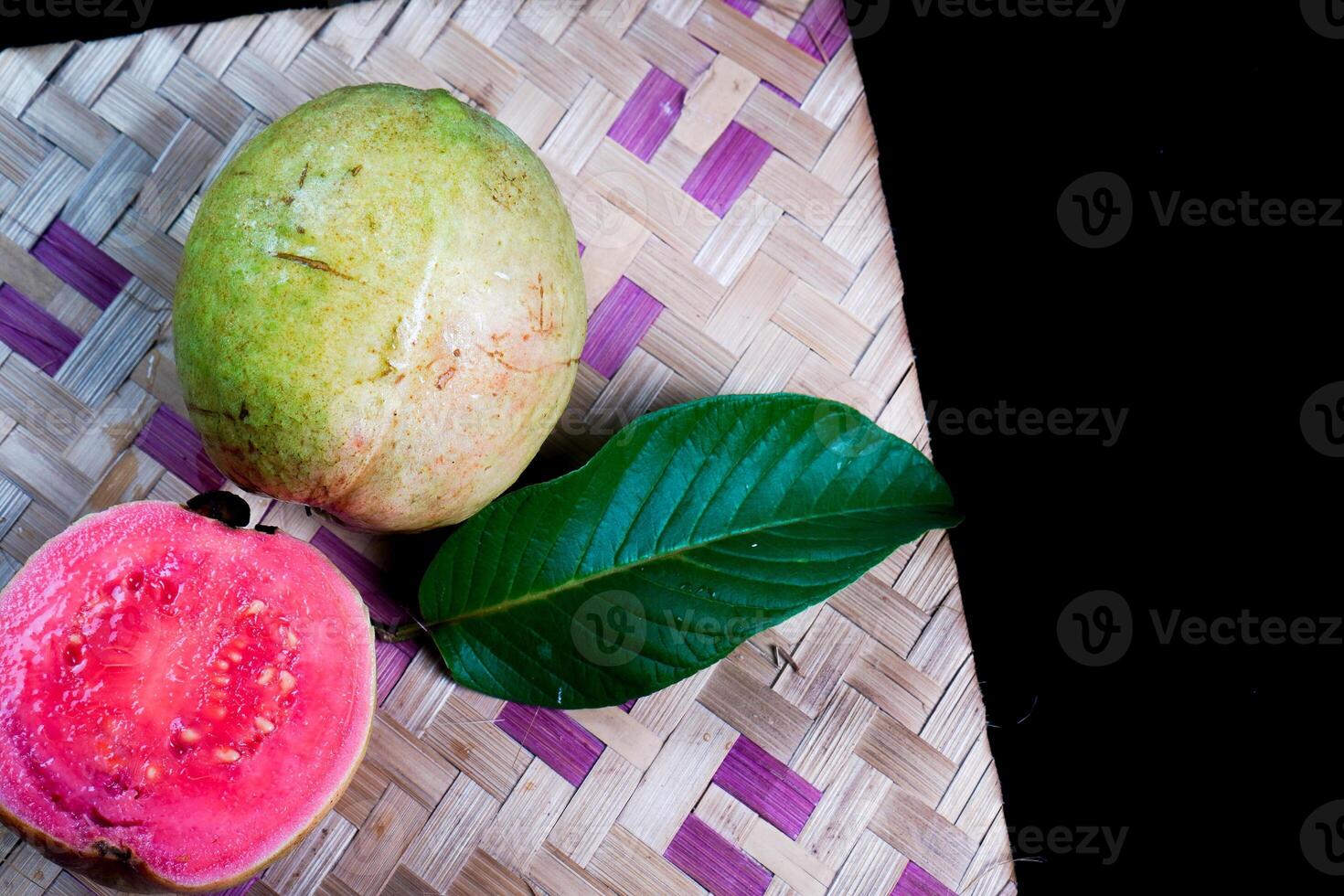 Guava isolated. Collection of red fleshed guava fruit with yellowish green skin and leaves isolated on black background with woven bamboo. photo
