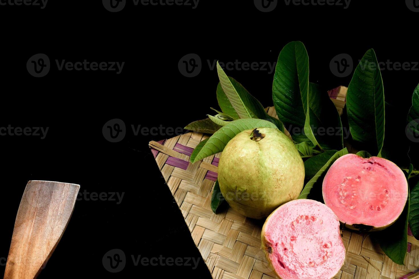 Guava isolated. Collection of red fleshed guava fruit with yellowish green skin and leaves isolated on black background with woven bamboo. photo