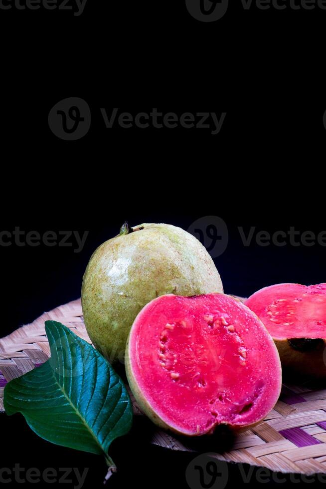 Guava isolated. Collection of red fleshed guava fruit with yellowish green skin and leaves isolated on black background with woven bamboo. photo