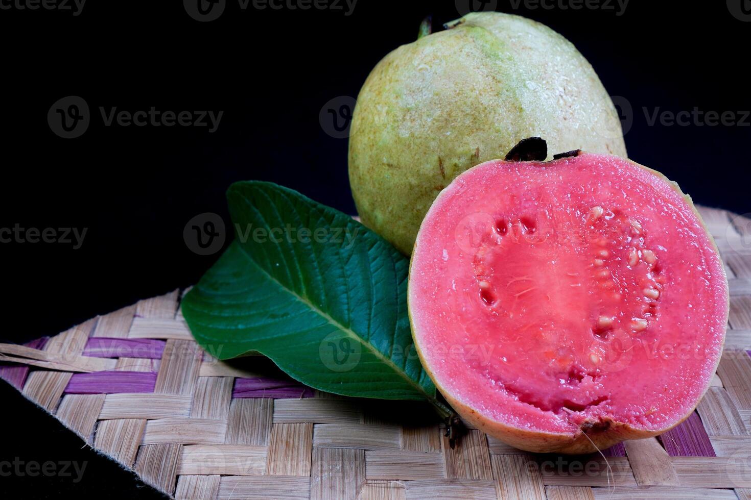 Guava isolated. Collection of red fleshed guava fruit with yellowish green skin and leaves isolated on black background with woven bamboo. photo